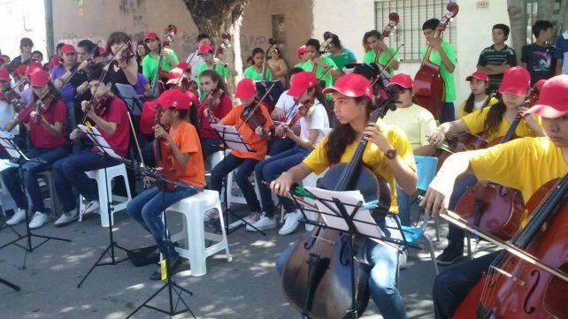 Una postal de orquesta de ni&ntilde;os, ni&ntilde;as y j&oacute;venes en un show al aire libre.