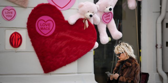 Una mujer revisa su teléfono junto a una tienda decorada con ositos de peluche y recortes en forma de corazón en Bucarest