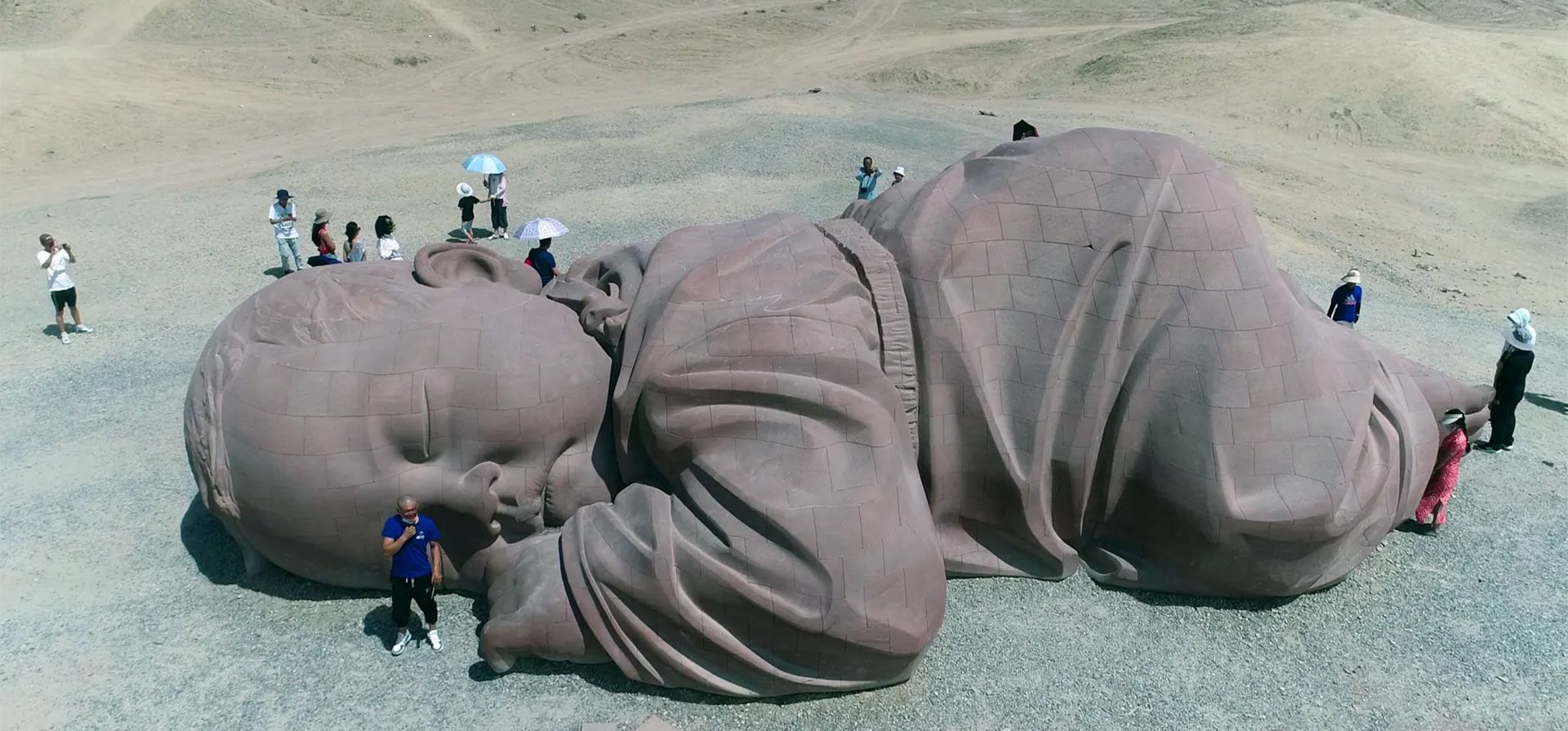 Jiuquan, China. Personas que visitan la escultura El Hijo de la Tierra, un enorme bebé dormido en el desierto de Gobi en la provincia de Gansu. Mide 15 metros de largo, 4,3 metros de alto y 9 metros de ancho, fue hecho de piedra arenisca roja utilizando tecnología 3D por el artista Dong Shubing. Fotografía: VCG/Getty Images