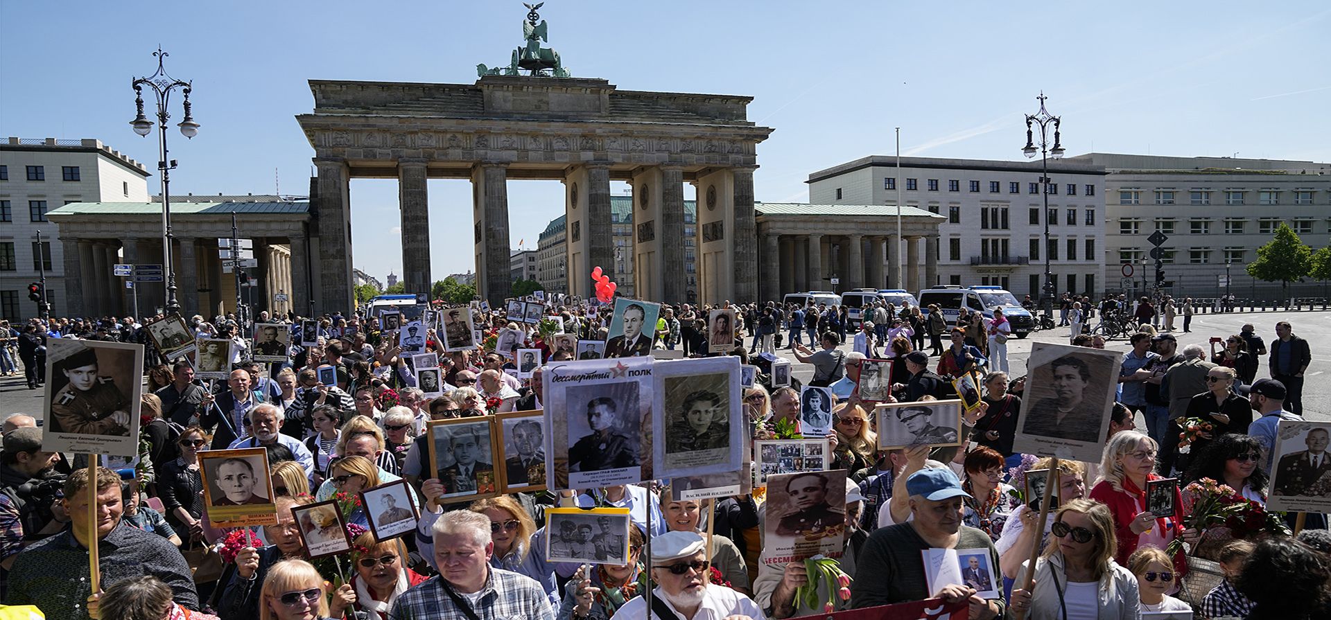 La gente porta retratos de familiares de la Unión Soviética que lucharon en la Segunda Guerra Mundial, durante la marcha del Regimiento Inmortal para conmemorar el final de la Segunda Guerra Mundial, con la Puerta de Brandenburgo al fondo, en Berlín, Alemania, el lunes 9 de mayo de 2022.