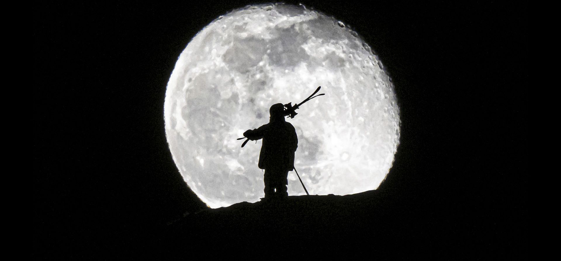 Un hombre lleva sus esquís durante la salida de la luna sobre el centro turístico alpino de Gryon, Suiza, el martes 7 de febrero de 2023. (Anthony Anex/Keystone vía AP)
