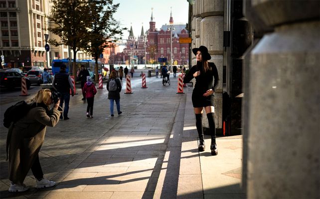 Una mujer posa para una producción fotográfica bajo un rayo de sol durante un cálido día de otoño en una calle cerca de la Plaza Roja con el Museo Histórico al fondo en Moscú, Rusia.