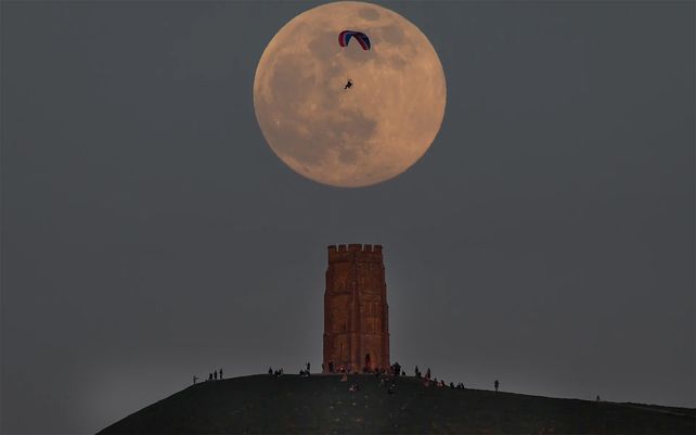 Un parapente vuela más allá de la luna llena cerca de Glastonbury Tor en Glastonbury
