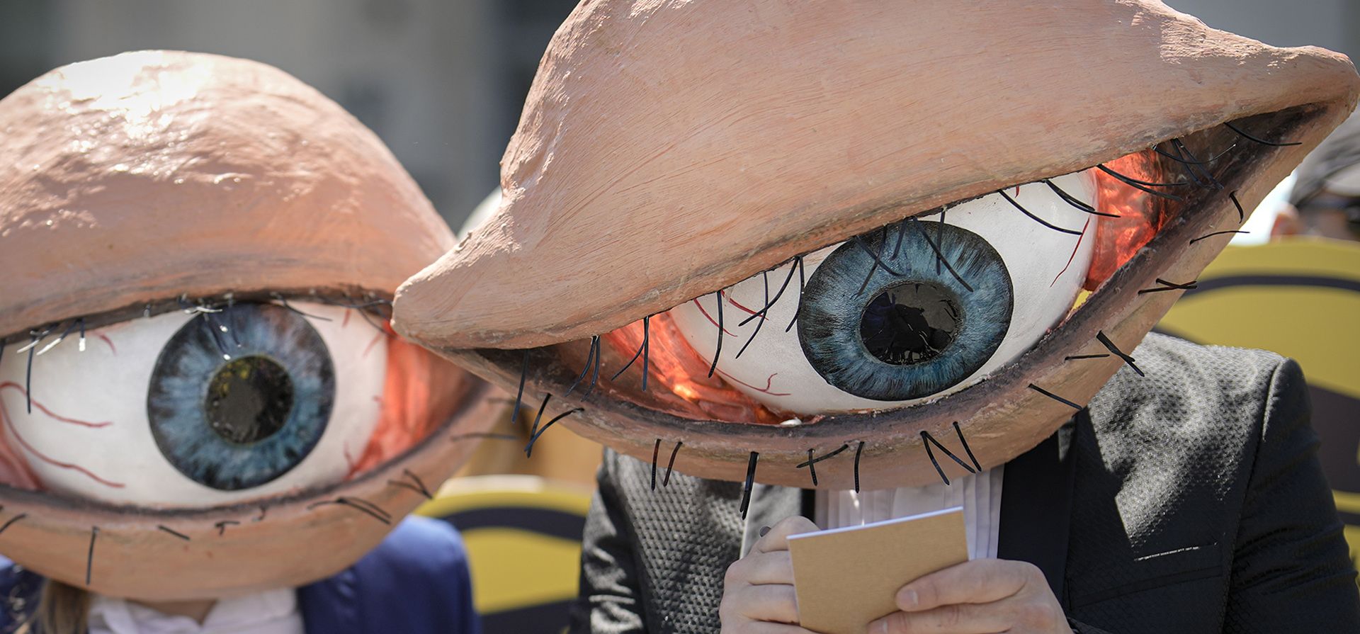 Activistas con máscaras que representan grandes globos oculares asisten a una protesta contra las actualizaciones planificadas de las leyes de seguridad nacional del país, luego de que se filtrara un borrador a los medios a principios de este mes, en Bucarest, Rumania, el miércoles 22 de junio de 2022. Decenas de activistas se reunieron fuera de la sede del gobierno para protestar contra los cambios propuestos a las leyes que ofrecen mayor poder al servicio de inteligencia de Rumania (SRI), que incluyen la obligación de que los ciudadanos y las empresas ofrezcan apoyo al servicio si así lo solicitan.