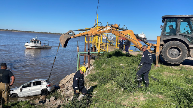 Bomberos de Fray Luis Beltrán con una pala mecánica intentan rescatar el auto del río.