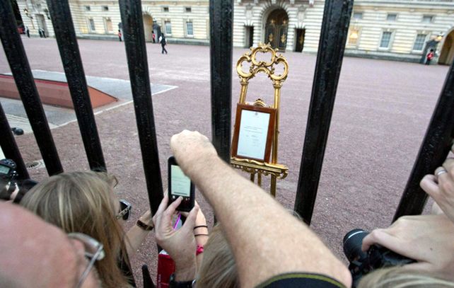 Curiosos se agolpan para fotografiar el anuncio oficial del nacimiento en un atril en la entrada del palacio de Buckingham.