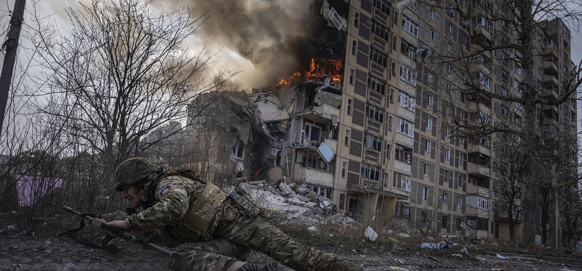 Un oficial de policía ucraniano se refugia frente a un edificio en llamas que fue alcanzado por un ataque aéreo ruso en Avdiivka, Ucrania. (Foto AP/Evgeniy Maloletka)