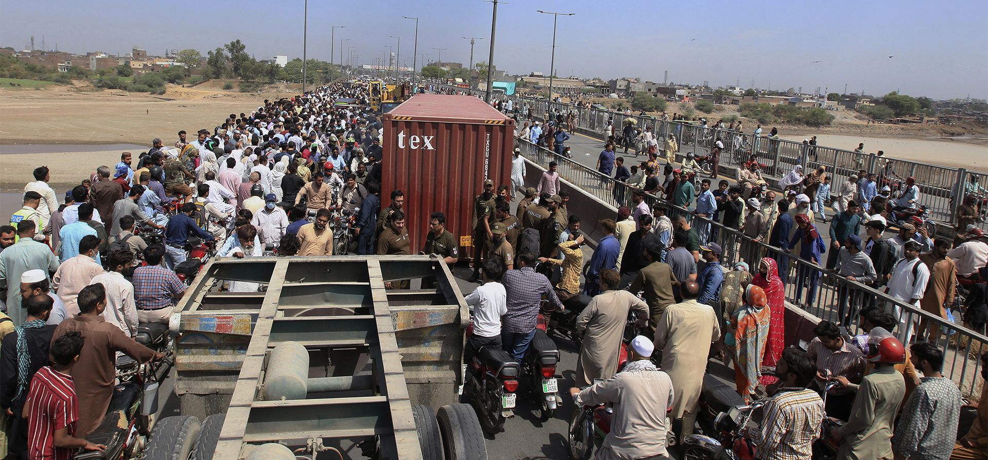 La gente cruza un puente sobre el río Ravi que está cerrado al tráfico debido a los contenedores colocados por las autoridades en un intento de frustrar una protesta planificada, en Lahore, Pakistán, el martes 24 de mayo de 2022.