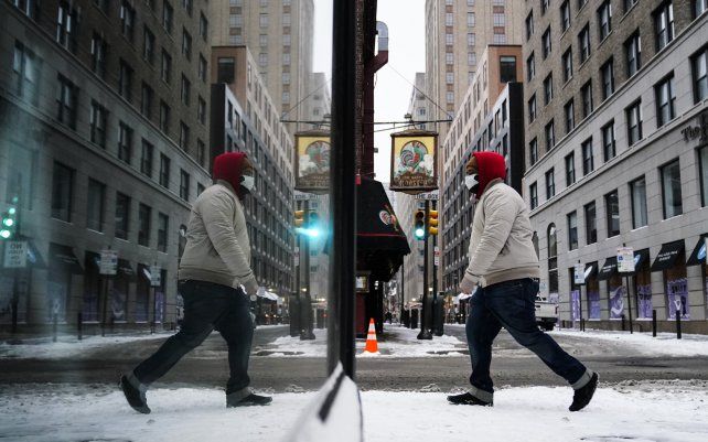 Una persona se refleja en una vidriera mientras camina durante una tormenta invernal en Filadelfia.