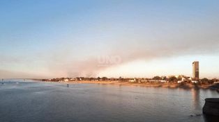 Postal de la gran columna de humo elevándose tras la costanera este de la ciudad.