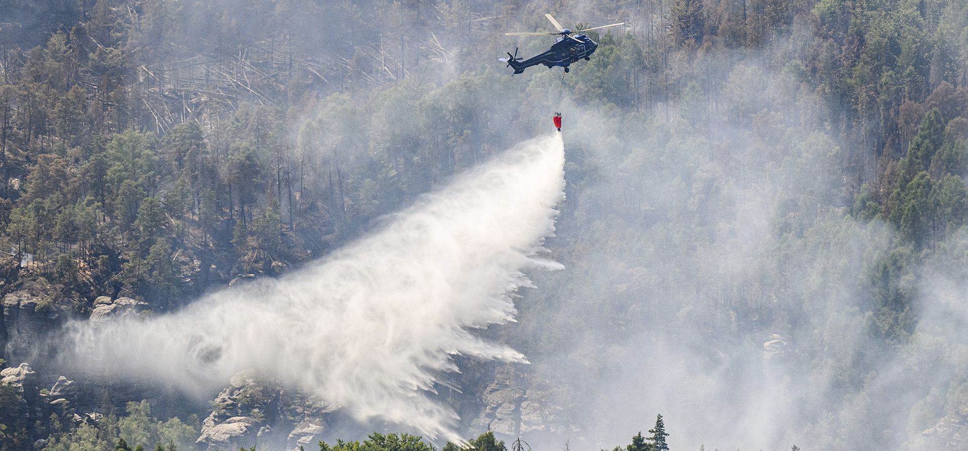 Un helicóptero de la Policía Federal Alemana vuela con un tanque de agua externo para extinguir un incendio forestal en el Parque Nacional de la Suiza Sajona en Schmilka, Alemania, el jueves 28 de julio de 2022.
