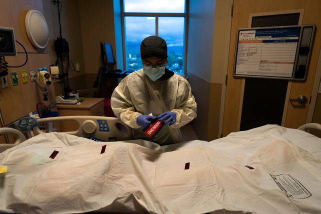 El enfermero Bryan Hofilena adhiere la etiqueta Paciente con Covid al cuerpo de un internado fallecido en el Providence Holy Cross Medical Center de los Angeles.&nbsp;