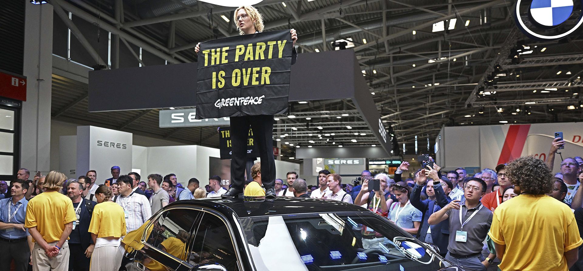 Un activista de Greenpeace se sube a un automóvil en exhibición y sostiene un cartel con el lema