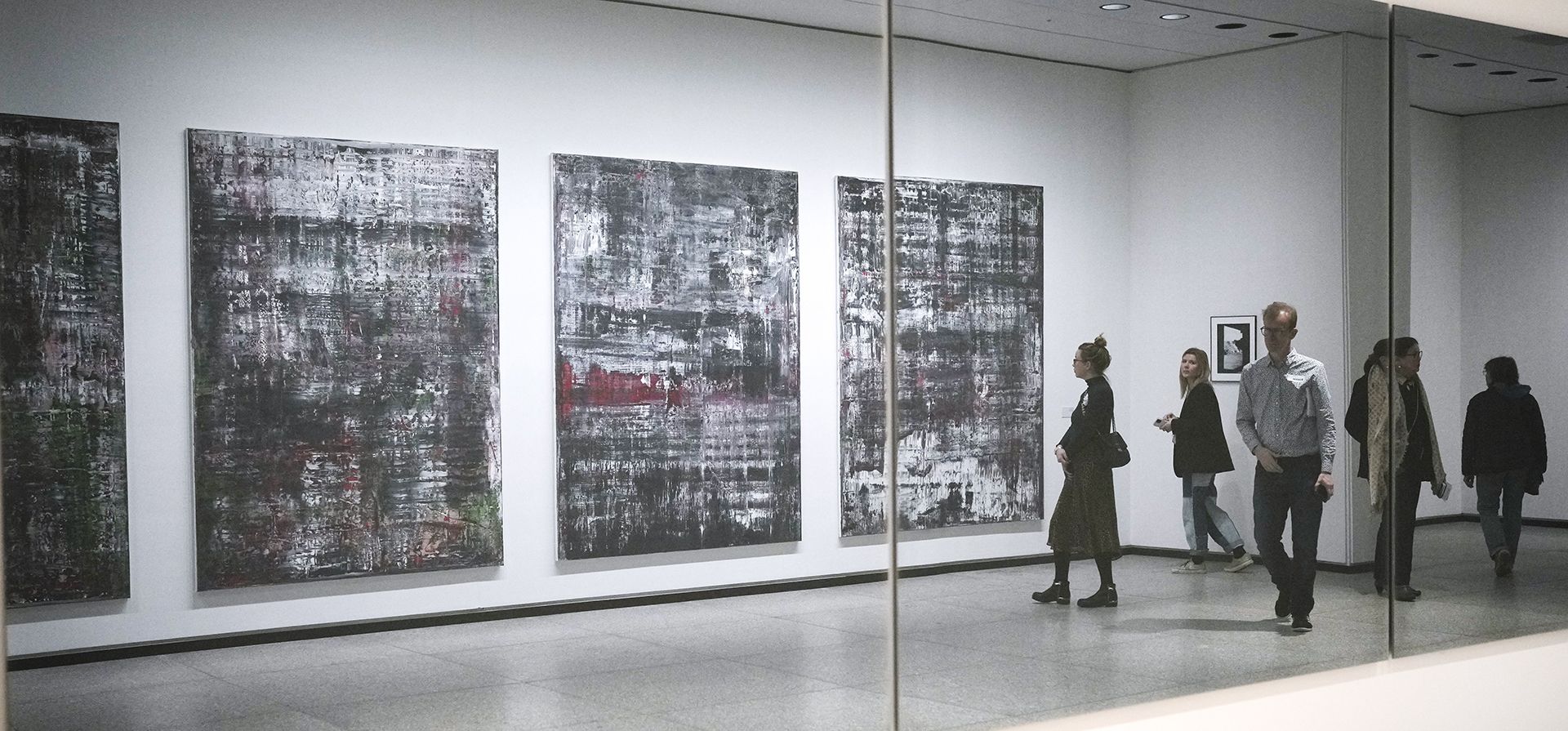 La gente se refleja en un espejo frente a las pinturas de