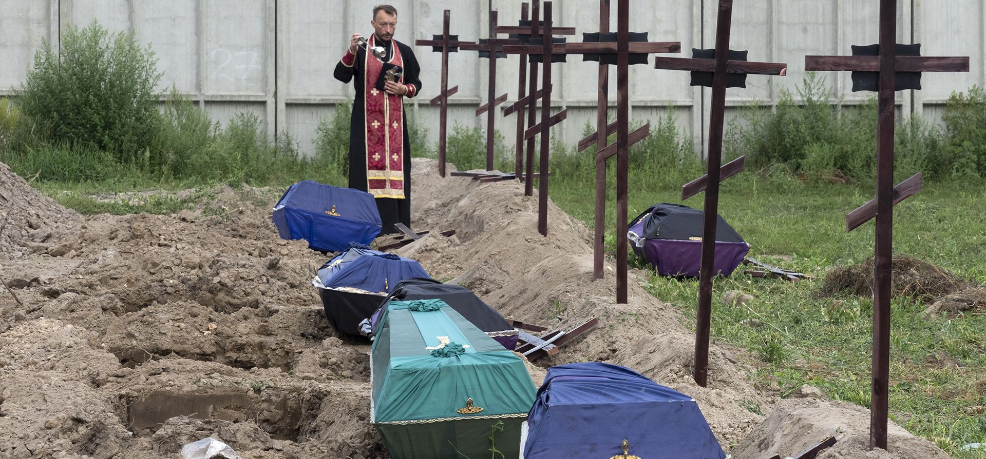 Un sacerdote reza por los civiles no identificados asesinados por las tropas rusas durante la ocupación rusa en Bucha, en las afueras de Kyiv, Ucrania, el jueves 11 de agosto de 2022. Once cuerpos no identificados exhumados de una fosa común fueron enterrados en Bucha este jueves.