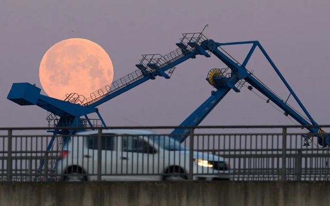 Un coche circula por el puente sobre el Flutrinne mientras se ve la Luna Super Rosa al fondo.