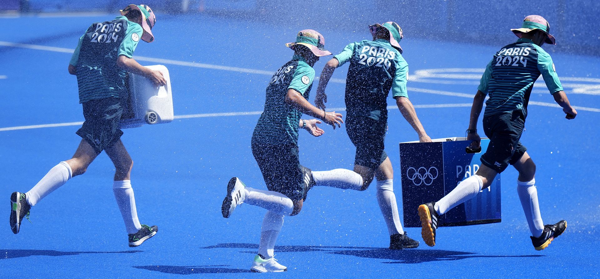 Los encargados de la pelota cruzan el campo mientras se rocía agua durante un descanso en el partido de semifinales de hockey sobre césped masculino entre Holanda y España en el Estadio Yves-du-Manoir durante los Juegos Olímpicos de Verano de 2024, el martes 6 de agosto de 2024, en Colombes, Francia. (Foto AP/Aijaz Rahi) Los encargados de la pelota cruzan el campo mientras se rocía agua durante un descanso en el partido de semifinales de hockey sobre césped masculino entre Holanda y España en el Estadio Yves-du-Manoir durante los Juegos Olímpicos de Verano de 2024, el martes 6 de agosto de 2024, en Colombes, Francia. (Foto AP/Aijaz Rahi)