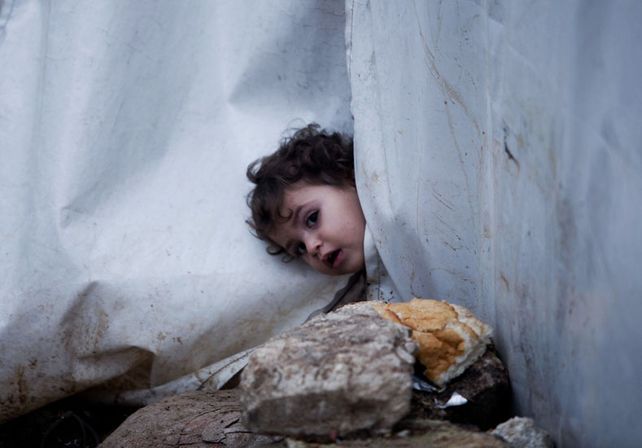 Una niña asoma la cabeza por la lona de su tienda de campaña en el campo de Azaz