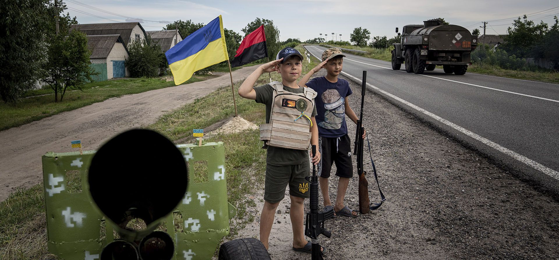 Niños al costado de una ruta saludan a los soldados ucranianos con pistolas de plástico mientras juegan en el puesto de control construido por ellos mismos en la carretera en la región de Kharkiv, Ucrania.