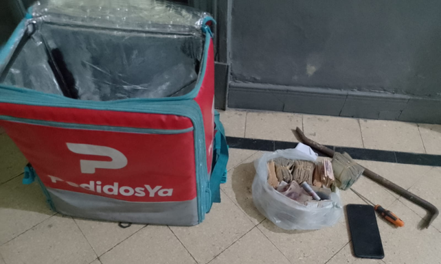 Uno de los ladrones llevaba una mochila de Pedidos Ya donde guardaba la barreta. Al lado el dinero sustraído de la caja registradora. 