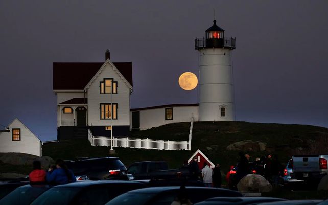 La superluna rosa se ve salir detrás del faro de Nubble en el Cabo Neddick