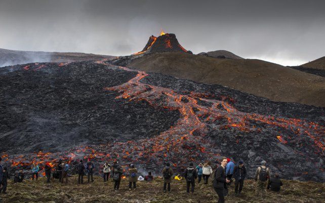La gente se toma fotos mientras la lava fluye de la erupción de un volcán en la península de Reykjanes, en el suroeste de Islandia. La última erupción volcánica de Islandia atrajo rápidamente a multitudes de personas que esperan acercarse y fotografiar a los suaves flujos de lava.