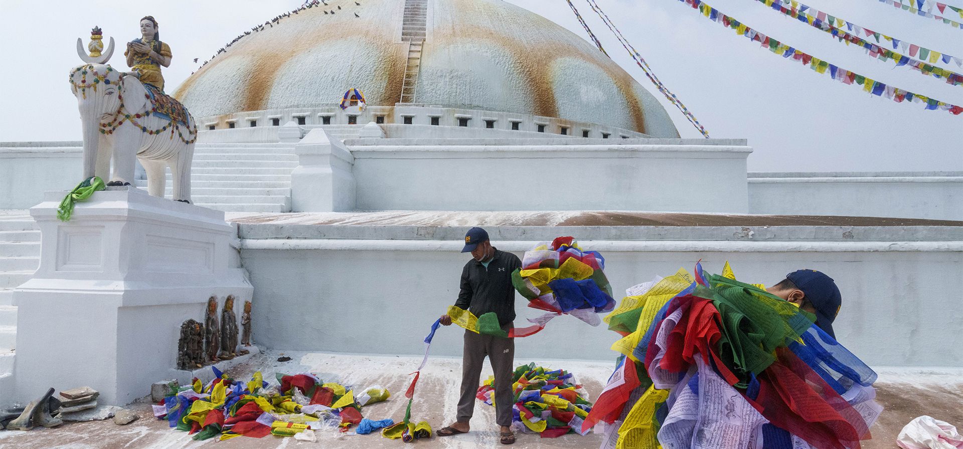 Hombres nepaleses cuelgan banderas de oración ofrecidas por devotos durante el festival Buddha Jayanti o Buddha Purnima en Boudhanath Stupa, Katmandú, Nepal, el lunes 16 de mayo de 2022. El festival marca los eventos triples de la vida de Gautama Buddha: el nacimiento, su iluminación y su logro de un estado de Nirvana que libera a los creyentes del círculo de la muerte y el renacimiento.