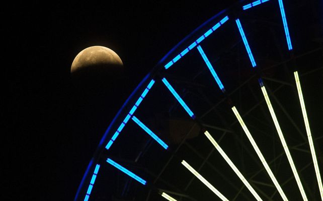 El avance del eclipse lunar se ve detrás de una noria sobre la playa de Santa Mónica en California. El primer eclipse lunar total en más de dos años coincide con una superluna de un gran espectáculo cósmico.&nbsp;