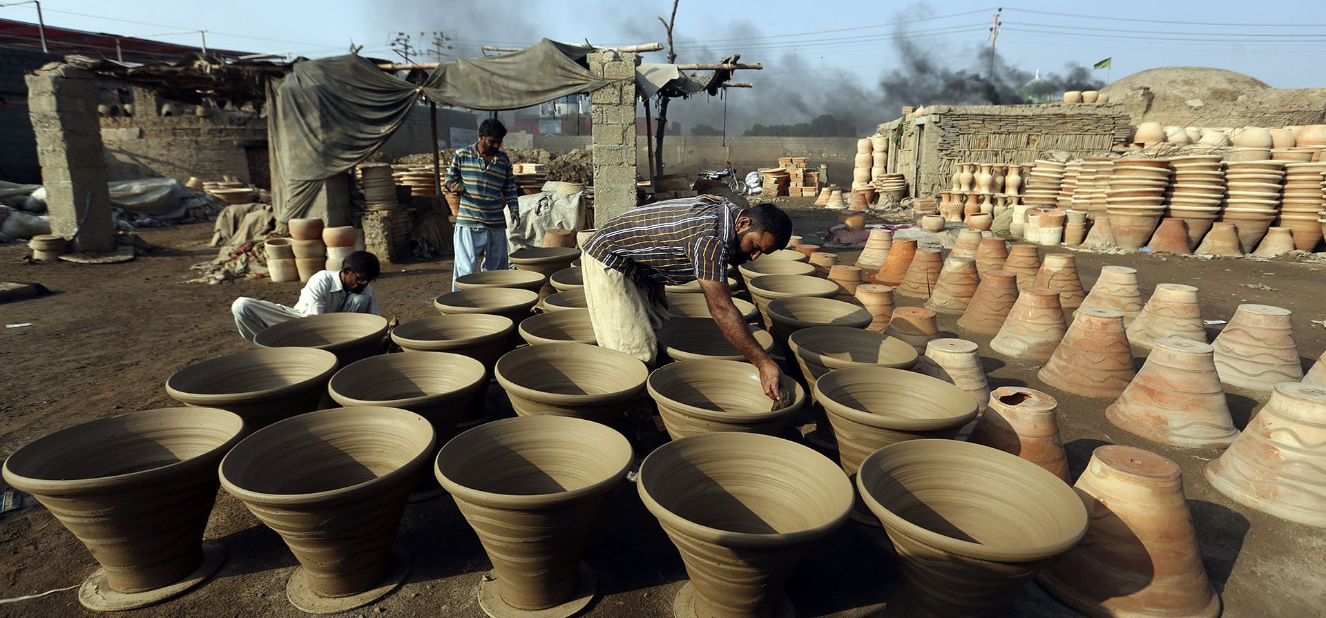 Un alfarero hace una vasija de barro mientras otros trabajadores revisan las vasijas en su taller en Karachi, Pakistán, el martes 8 de noviembre de 2022.