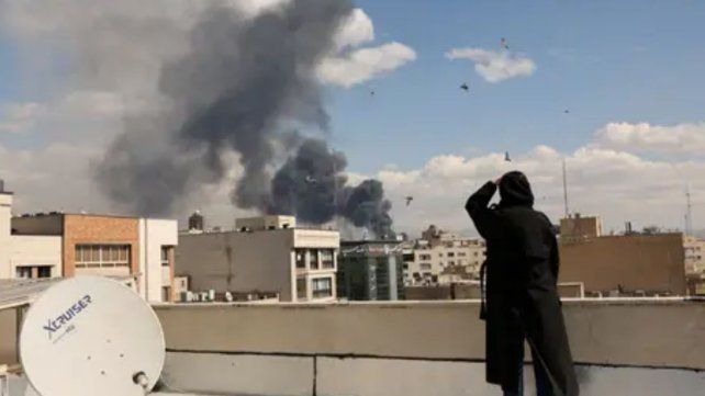 Impacto en la capital de Irán: una civil observa desde una terraza las columnas de humo tras los ataques aéreos de Israel sobre centros estratégicos en Teherán.