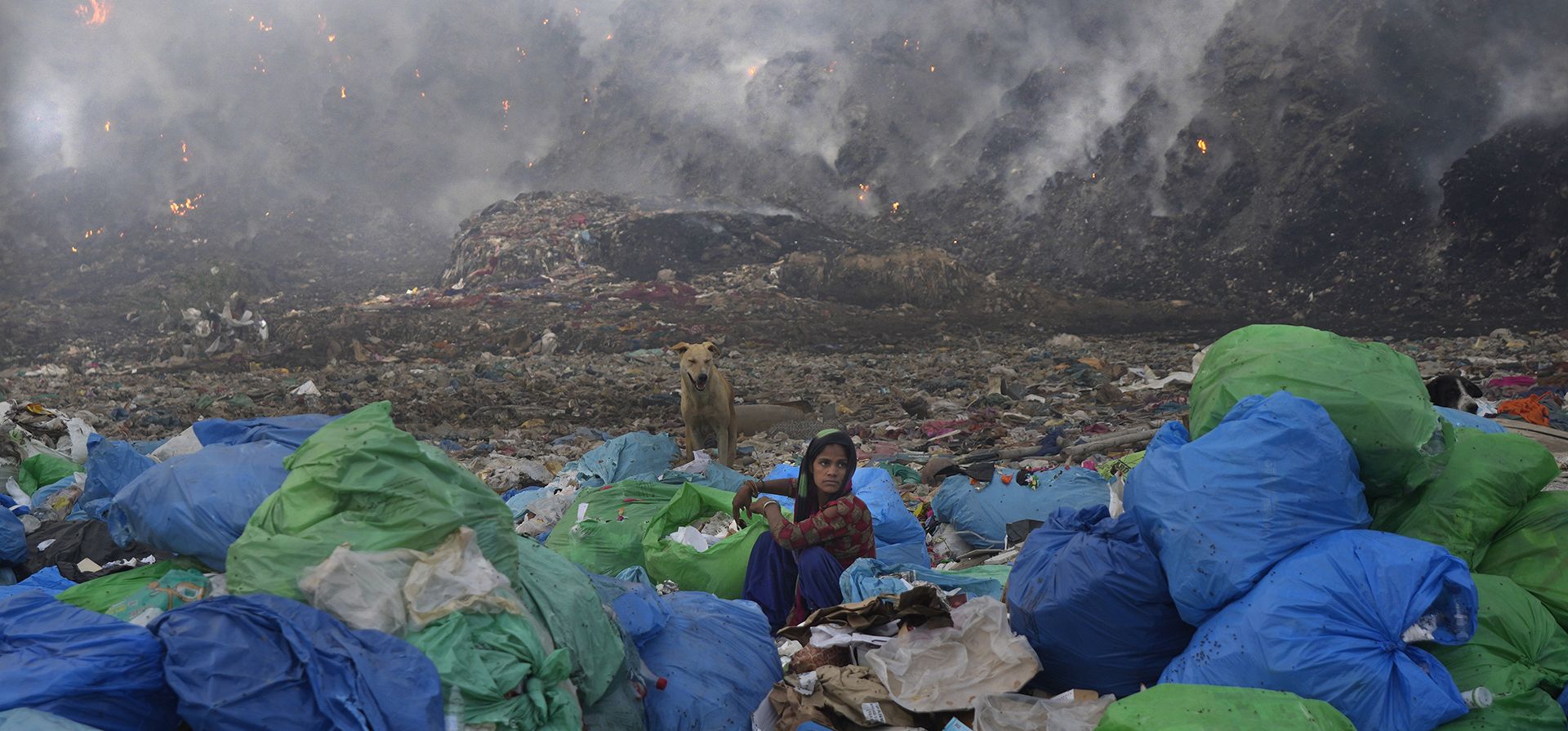 Nueva Delhi, India. Un trapero clasifica los artículos en un vertedero mientras un incendio descontrolado arde en el fondo.