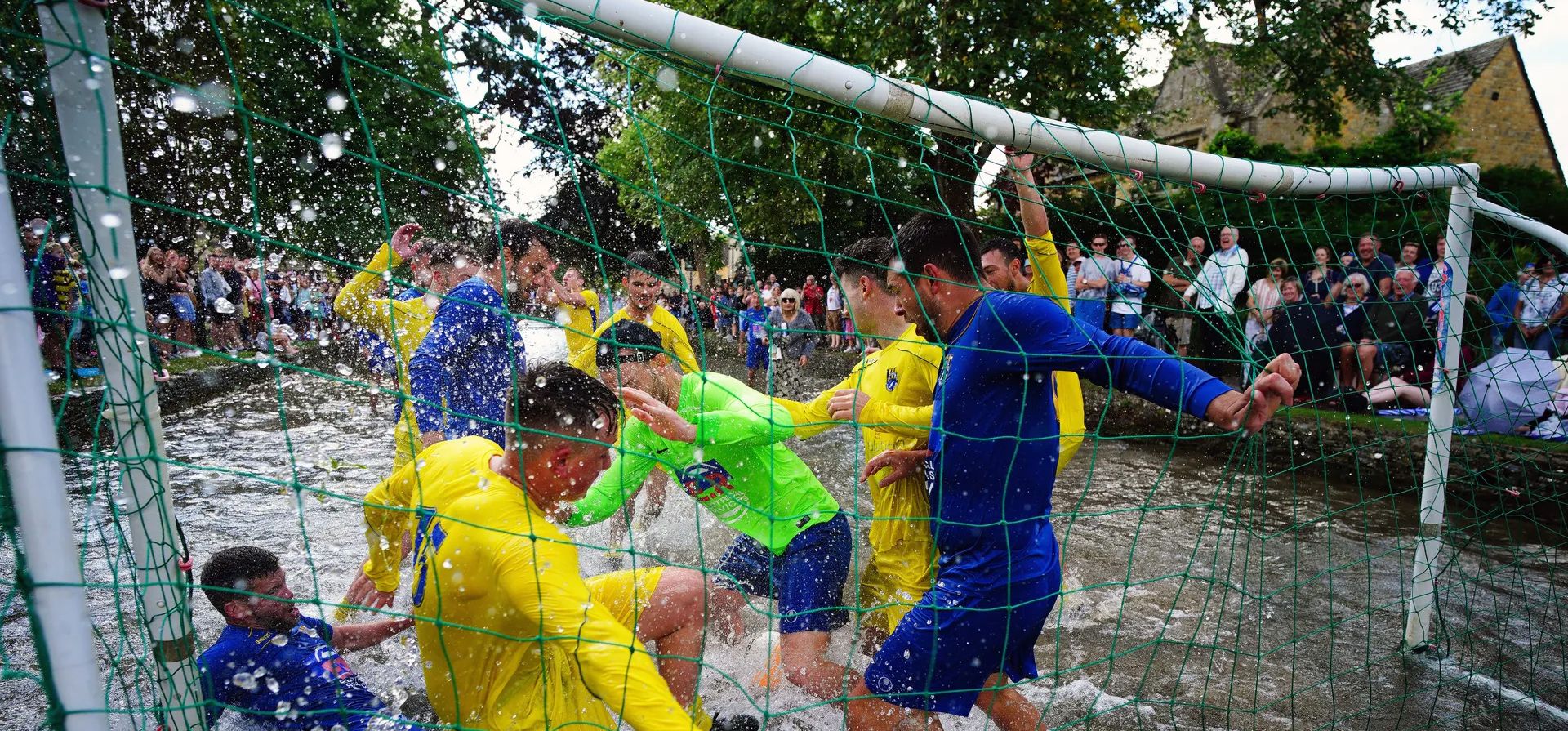 Futbolistas de Bourton Rovers disputan el balón durante el tradicional partido de fútbol anual River Windrush, que se lleva a cabo durante más de 100 años, en el pueblo de Bourton-on-the-Water, Inglaterra, en los Cotswolds, el lunes 28 de agosto de 2023. (Ben Birchall/PA vía AP)