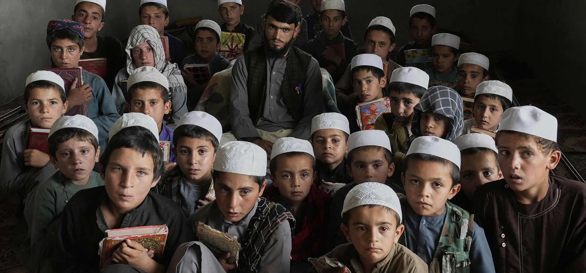 Niños afganos posan para una foto con su maestra durante una clase de Corán en la escuela religiosa Abdullah Ibn-Masoud, en las afueras de Kabul, Afganistán, el martes 5 de agosto de 2025. (Foto AP/Ebrahim Noroozi)