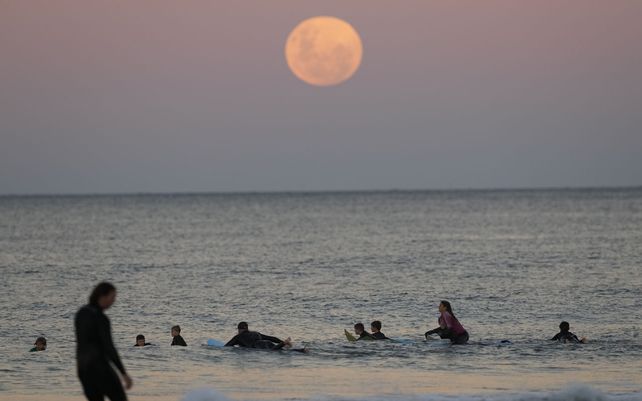 Los surfistas esperan las olas mientras la luna sale en Sydney. Un eclipse lunar total