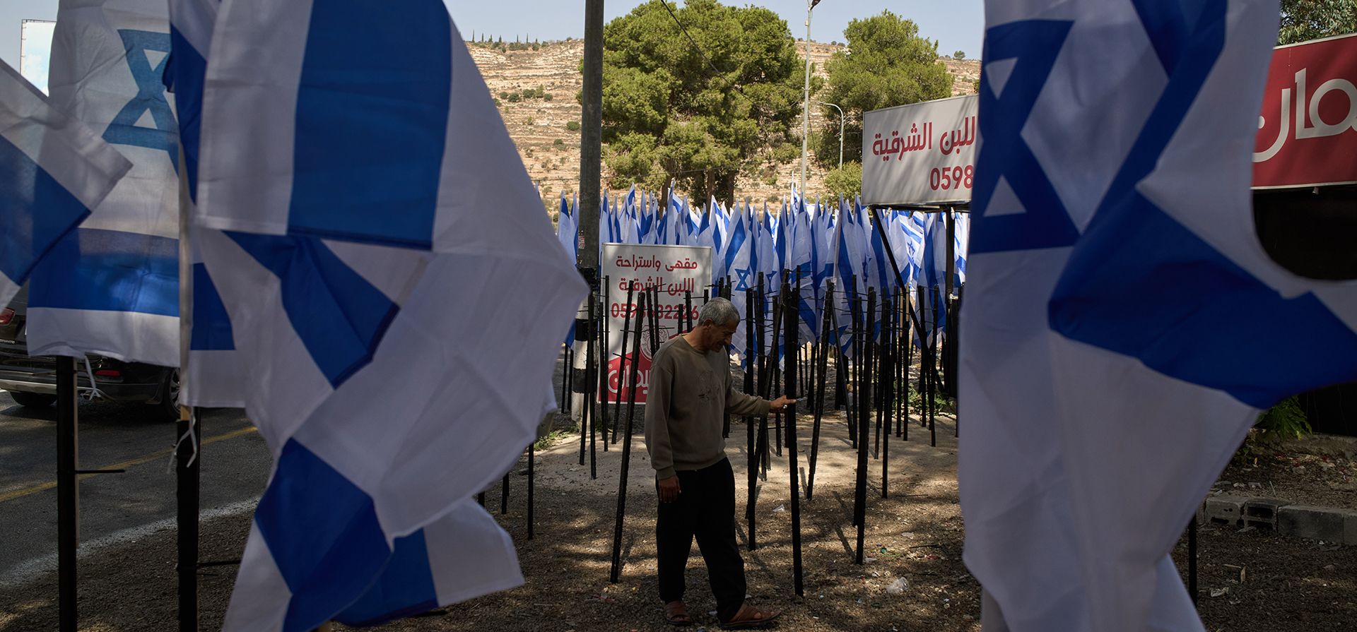 El comerciante palestino Mouayad Oweis permanece frente a su negocio, situado a pie de carretera, después de que colonos israelíes colocaran decenas de banderas de Israel que bloqueaban el acceso a su tienda en la localidad de al-Lubban al-Sharqiya, en Cisjordania, el jueves 8 de octubre de 2026. (Foto AP/Leo Correa) El comerciante palestino Mouayad Oweis permanece frente a su negocio, situado a pie de carretera, después de que colonos israelíes colocaran decenas de banderas de Israel que bloqueaban el acceso a su tienda en la localidad de al-Lubban al-Sharqiya, en Cisjordania, el jueves 8 de octubre de 2026. (Foto AP/Leo Correa)