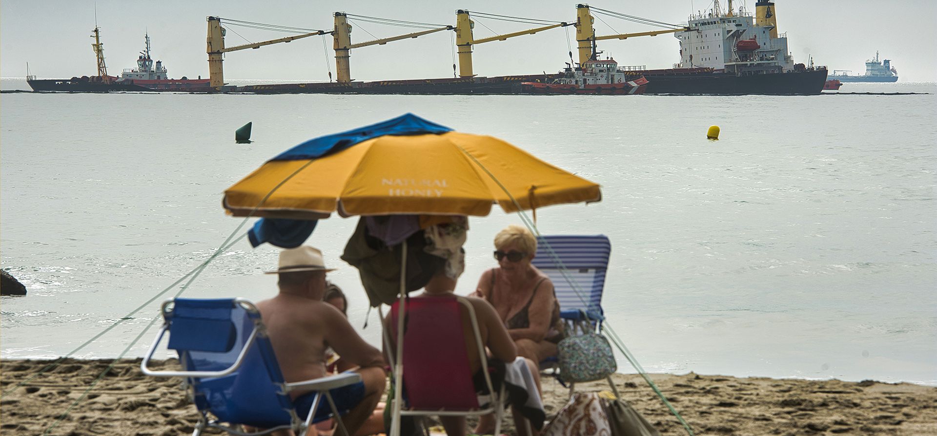 Un grupo de personas se sienta en una playa frente al buque de carga OS 35 registrado en Tuvalu que yace en el lecho marino frente a Gibraltar, el martes 30 de agosto de 2022. Las autoridades de Gibraltar dicen que han varado un buque de carga para evitar que se hunda después de que chocó con un carguero de gas natural licuado la madrugada del martes en la bahía de Gibraltar.