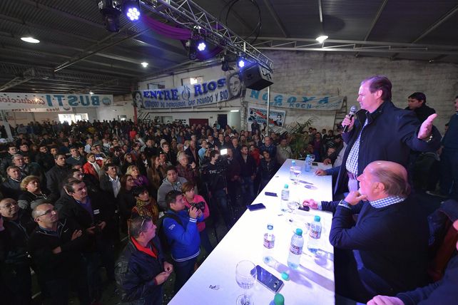 Bordet hablando parado y Busti sentado escuchando frente a la gente.&nbsp;
