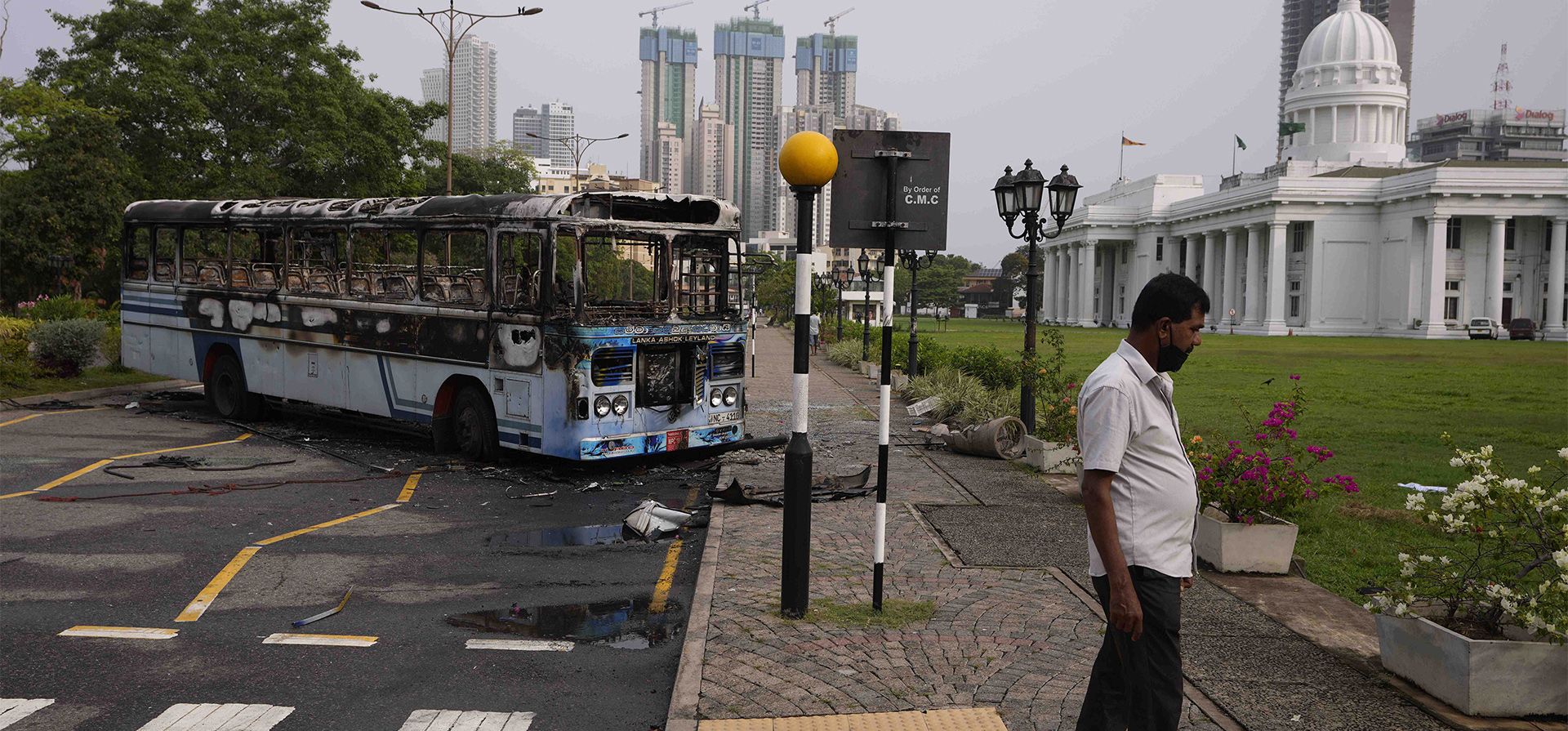 Un hombre de Sri Lanka camina por la acera cerca de un autobús quemado un día después de los enfrentamientos entre simpatizantes del gobierno y manifestantes antigubernamentales en Colombo, Sri Lanka, el martes 10 de mayo de 2022. Desafiando el toque de queda nacional en Sri Lanka, varios cientos de manifestantes continuaron con sus consignas contra el gobierno.