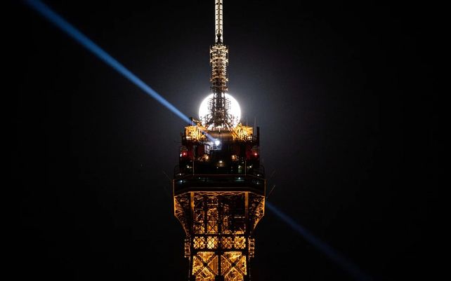 La luna llena se eleva sobre la Torre Eiffel en París.