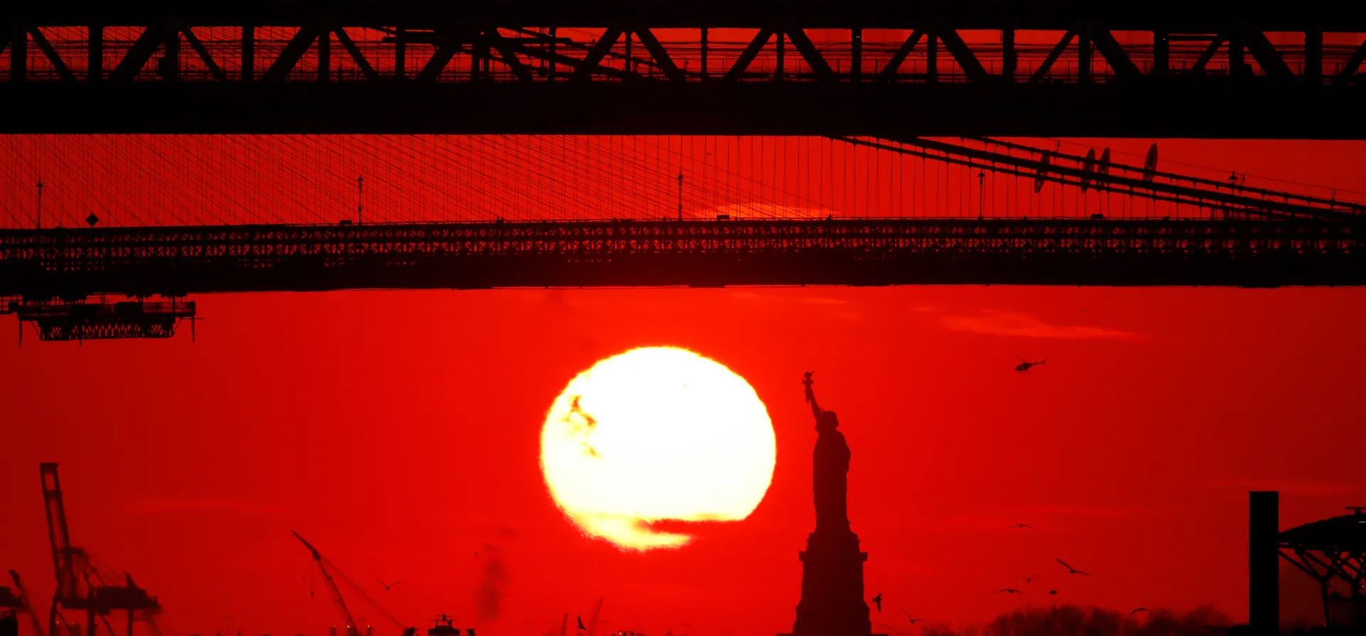 Nueva York, EE. UU. El sol se pone detrás de la Estatua de la Libertad, entre el Puente de Brooklyn y el Puente de Manhattan.