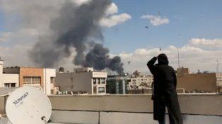 Impacto en la capital de Irán: una civil observa desde una terraza las columnas de humo tras los ataques aéreos de Israel sobre centros estratégicos en Teherán.