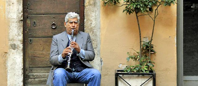 Un hombre toca el clarinete en busca de que alguien se apiade y le deje unas míseras monedas. Al lado un local comercial debió cerrar sus puertas por falta de clientes.