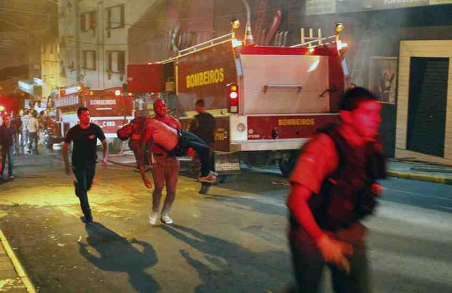 Un hombre carga a un herido en medio de bomberos que acuden a asistirlo. (Foto: AP)