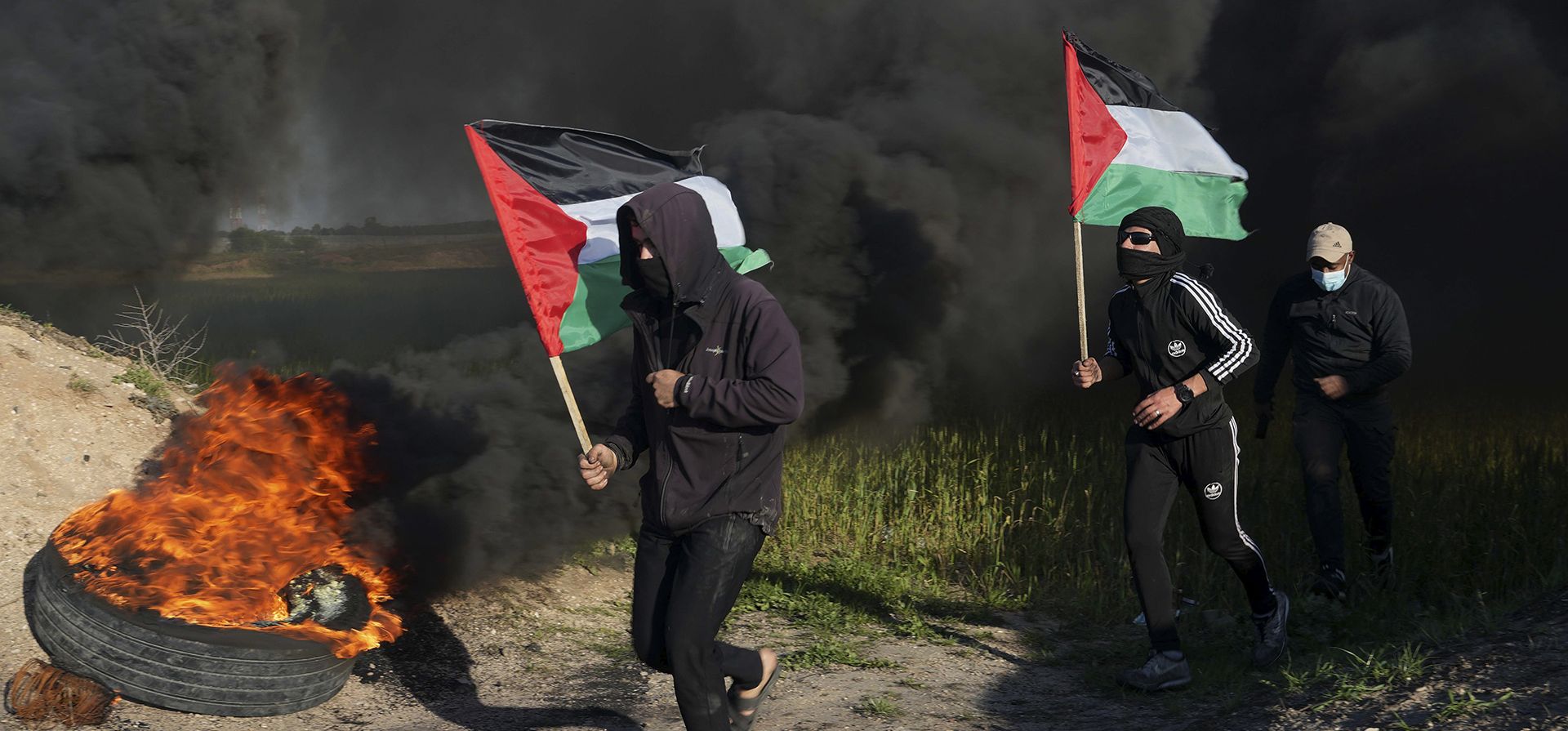 Manifestantes corren junto a neumáticos en llamas mientras portan banderas nacionales durante una protesta contra una redada militar israelí en la ciudad de Naplusa, en Cisjordania, a lo largo de la valla fronteriza con Israel, al este de la ciudad de Gaza, el miércoles 22 de febrero de 2023. (Foto AP/Adel Hana)