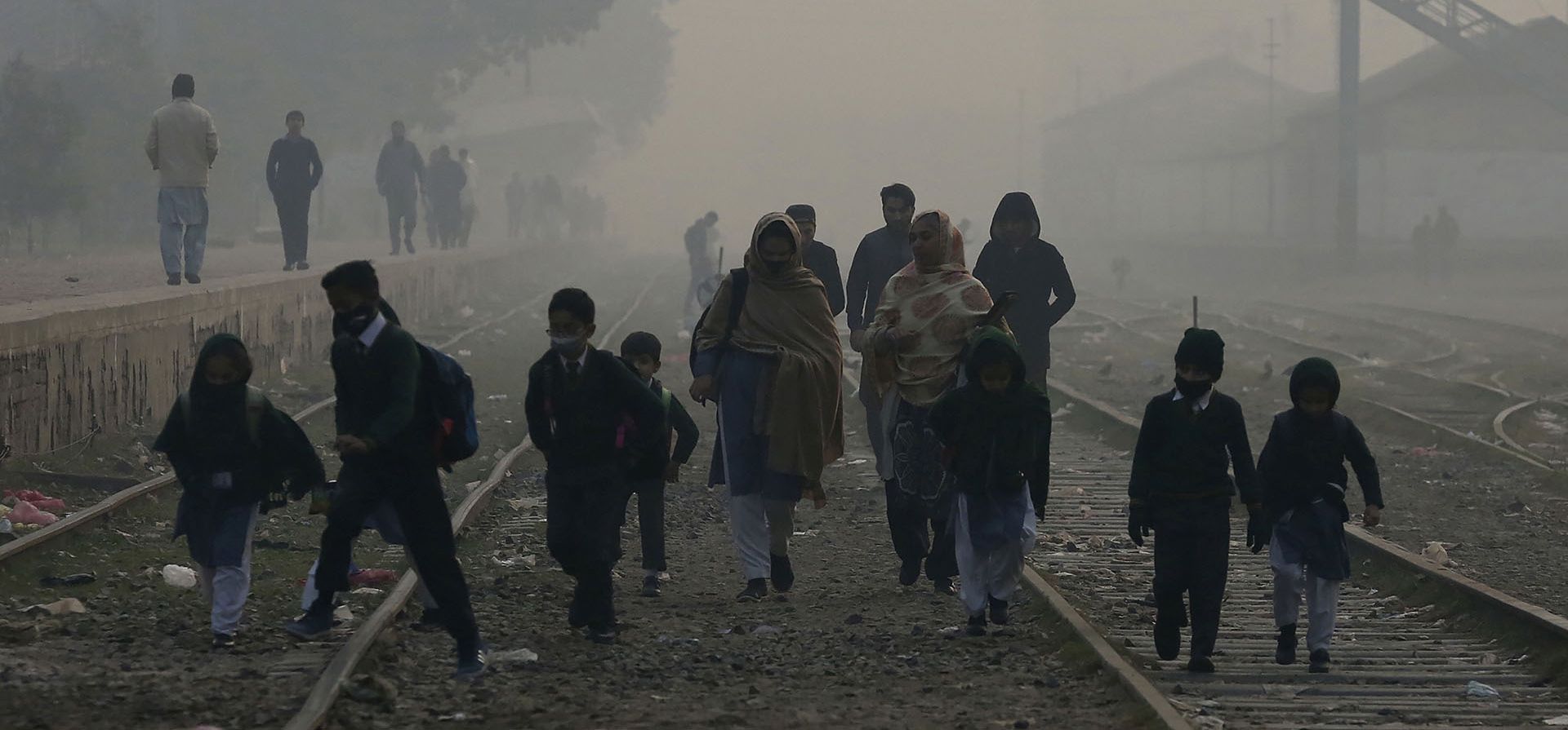 Los estudiantes caminan hacia su escuela a través de las vías del tren mientras la densa niebla reduce la visibilidad, en Peshawar, Pakistán, el miércoles 21 de diciembre de 2022. (Foto AP/Muhammad Sajjad)