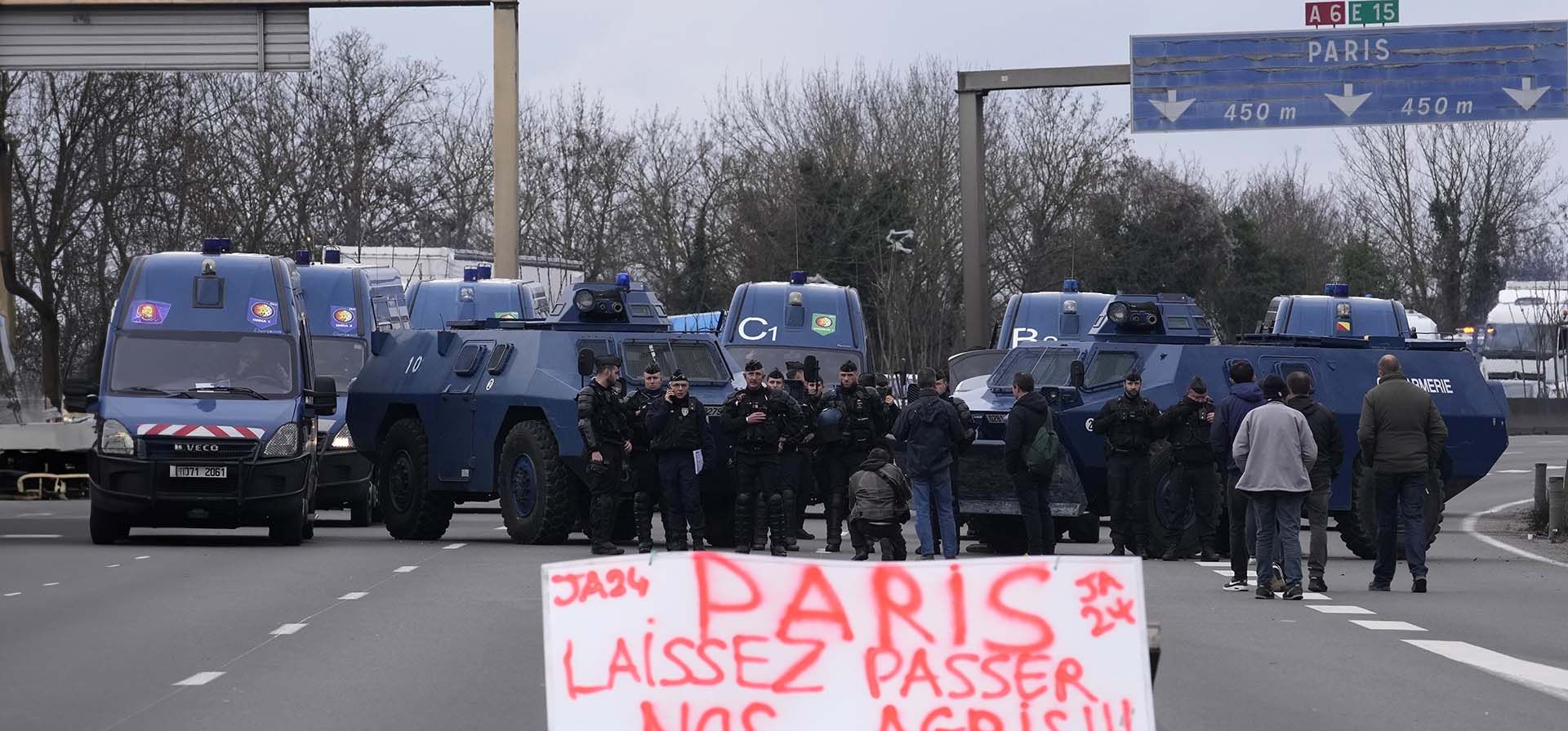 Un cartel dice "París, deja pasar a nuestros agricultores" mientras gendarmes con vehículos blindados se enfrentan a los manifestantes y sus tractores que bloquean una carretera, el miércoles 31 de enero de 2024 en Chilly-Mazarin, al sur de París. (Foto AP/Christophe Ena) Un cartel dice "París, deja pasar a nuestros agricultores" mientras gendarmes con vehículos blindados se enfrentan a los manifestantes y sus tractores que bloquean una carretera, el miércoles 31 de enero de 2024 en Chilly-Mazarin, al sur de París. (Foto AP/Christophe Ena)