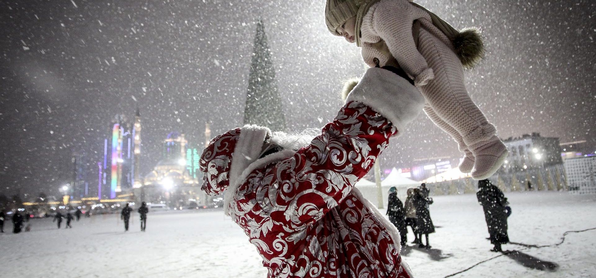 Una persona vestido como Santa Claus, juega con un niño durante la nevada en una plaza de Grozny. principal punto de atracción de la ciudad para las celebraciones de Año Nuevo, en Rusia. Foto: AP