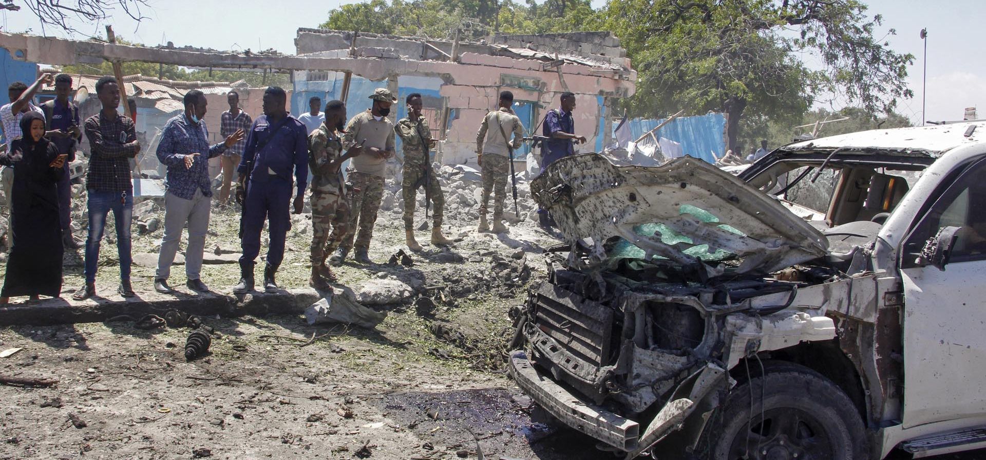 Las fuerzas de seguridad observan los restos de un vehículo blindado golpeado por una explosión en Mogadiscio, Somalia el miércoles 12 de enero de 2022. El miércoles se informó de una gran explosión fuera del aeropuerto internacional de la capital de Somalia y un socorrista dijo que hubo muertos y heridos.