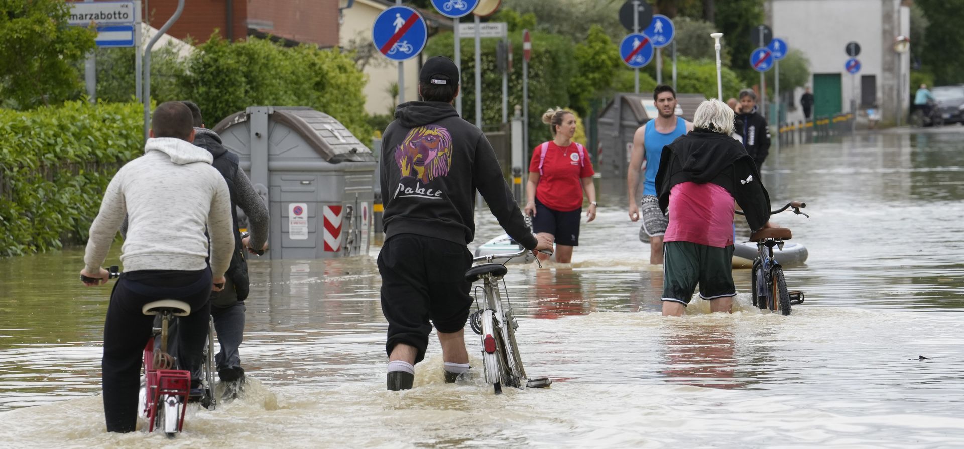 La gente pedalea en una calle inundada en Barbiano di Cotignola, Italia, el jueves 18 de mayo de 2023. Lluvias excepcionales del miércoles en una región del norte de Italia afectada por la sequía desbordaron los ríos. (Foto AP/Luca Bruno)