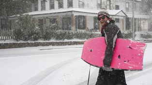 Un joven camina por calles cubiertas de nieve con una tabla de bodyboard el martes 21 de enero de 2025 en Pensacola, Florida. (Luis Santana/Tampa Bay Times vía AP)